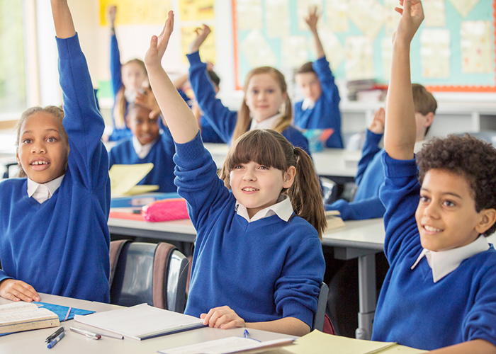 School pupils wearing blue uniforms with raised hands in a classroom