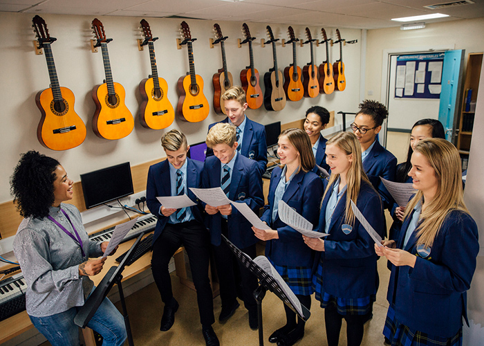 Pupils and a teacher in a music room with guitars and keyboards in the background