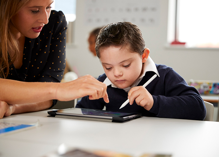 A child using a tablet being helped by a teacher