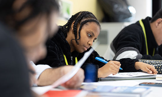 A focused shot on one child writing with other children blurred in the background