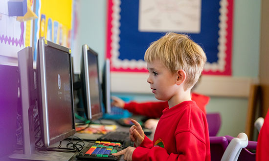 A young blonde child in a red jumper interacting with a computer