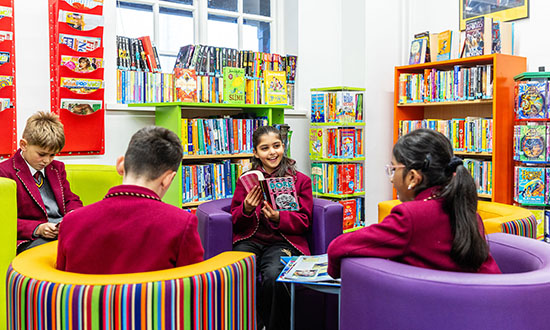 A group of four children interacting in a library on bright colourful chairs