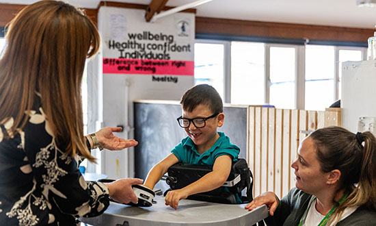 A child in a wheelchair interacting with two adults smiling