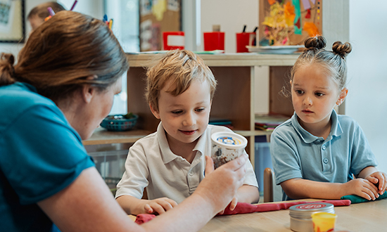 A teacher showing two children a container