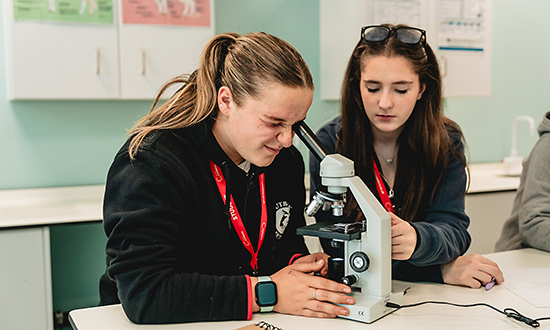 A student looking through a microscope alongside another woman