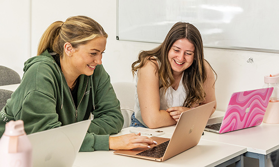 Two smiling women sitting at desks with laptops