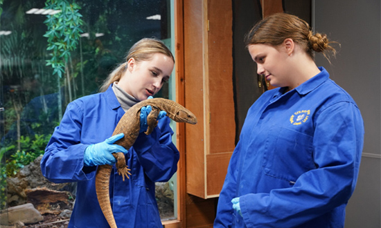 Two female students, one holding a reptile