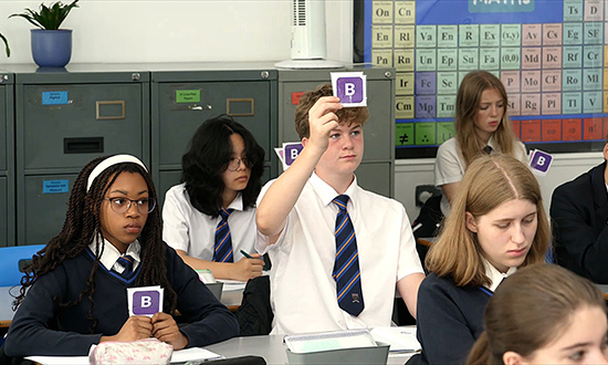 School pupils in a classroom holding up cards with letters printed on them