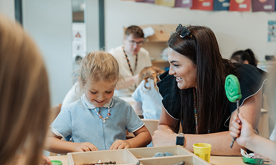 A young child playing at a table being supervised by an adult