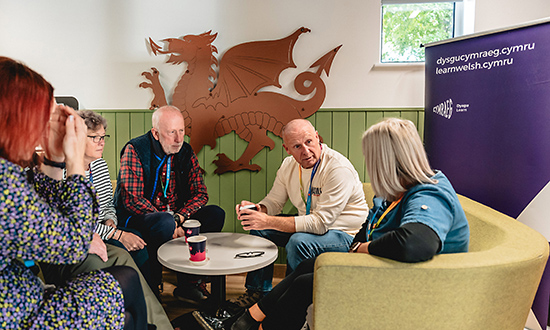 A group of adults sitting around a small table with a Welsh dragon in the background
